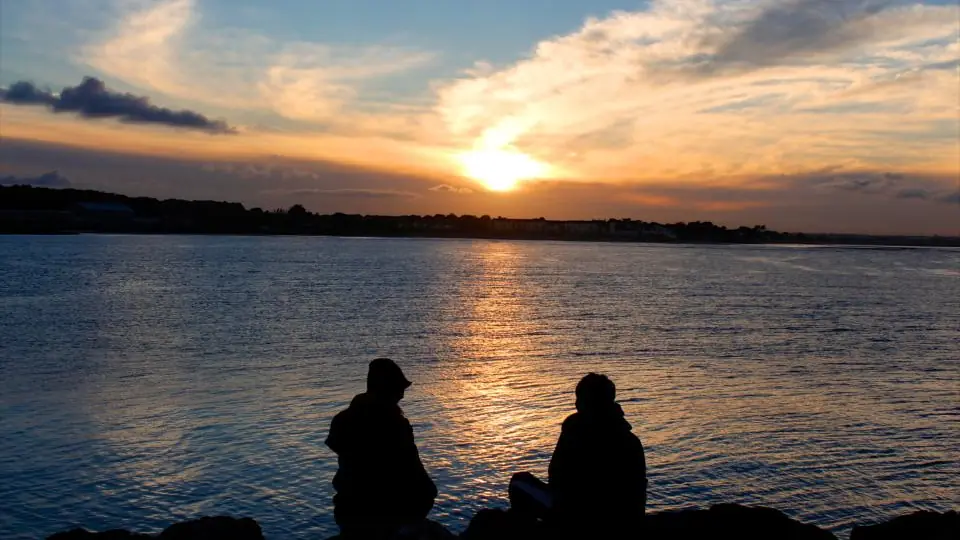 Sexdate Wallis: Paar schaut dem Sonnenuntergang am Wasser zu